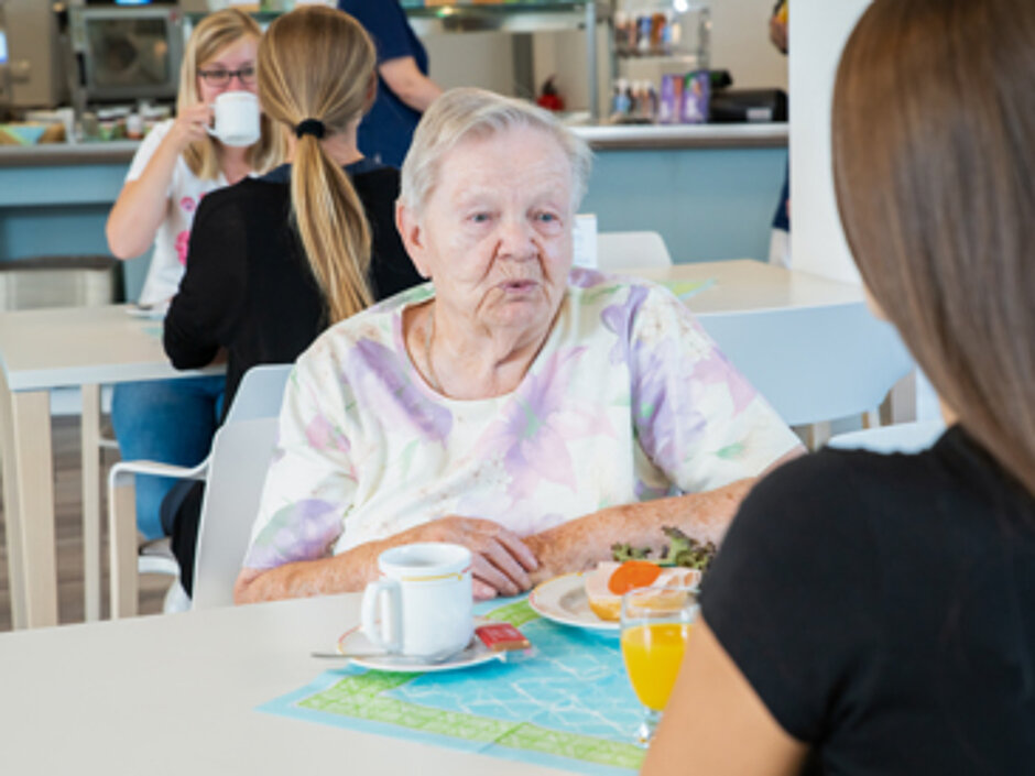 Eine Bewohnerin im Cafe. Sie ist im Gespräch mit einer Besucherin.