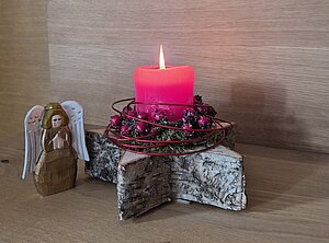 Ein Adventsgesteck mit roten Beeren und einer brennenden roten Kerze.